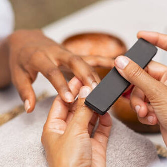 Close up of african hands of a qualified manicurist filing the nails of a young woman. Hands during manicure care session. Detail of a girl in a nail salon receiving manicure.