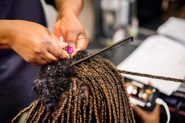 Close-up of a hairstylist hands making braids and doing hair extension to her client in salon